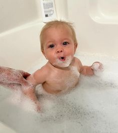 a baby sitting in a bathtub with bubbles on it's face and body