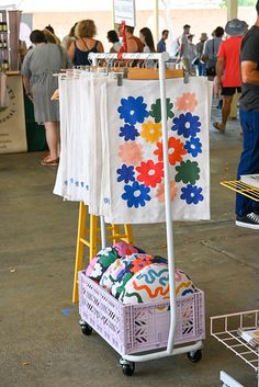 people are shopping at an outdoor market with clothing on racks and baskets in the foreground