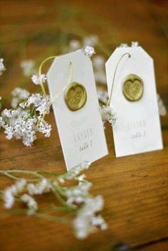 two white tags with gold buttons on them are sitting next to some baby's breath flowers