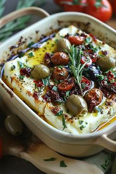 a dish with olives, tomatoes and cheese in it on a table next to other vegetables