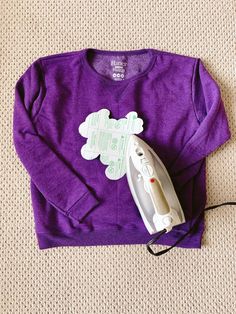 a purple shirt with a white teddy bear cut out on it and an electric iron laying next to it