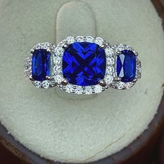 Top of ring height: 1.8mm Top of ring width: 2.8mm Shank width: 3.1mm  Stone material: blue & clear cubic zirconia Center stone size: 8mm  Stone shape: cushion cut (center) & round Center stone carat weight: 3.1 ct. Total number of CZ stones: 42 Stone setting: prong setting Metal: 925 sterling silver Plating: rhodium plated Finish: high polish Three Stone Engagement Rings Halo, Stone Material, Stone Setting, Cz Ring, Halo Engagement Ring, Silver Blue, Cz Stone, Three Stone, Cushion Cut