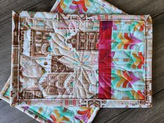 two quilted placemats sitting on top of a wooden table next to each other