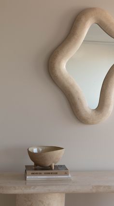 a white bowl sitting on top of a table next to a wall mounted round mirror