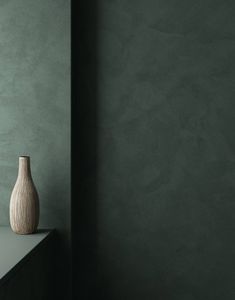 a white vase sitting on top of a table next to a green wall and shelf