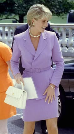 the woman is wearing a purple suit and holding a white purse while standing next to another woman