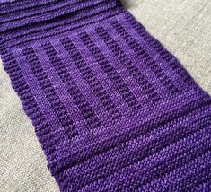 a purple knitted scarf laying on top of a bed