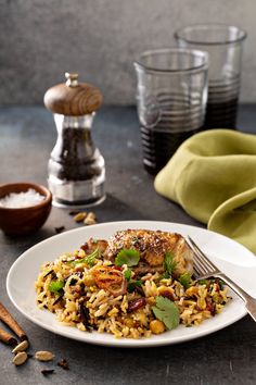 a white plate topped with rice covered in meat and veggies next to spices