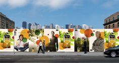 people walking past an advertisement on the side of a building with buildings in the background