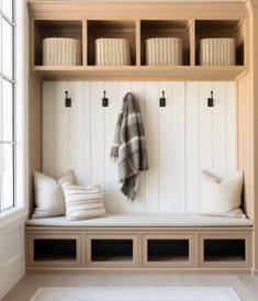 a white bench with pillows and blankets on it next to a window in a room