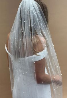 a woman wearing a wedding veil with pearls on the bottom and back of her head