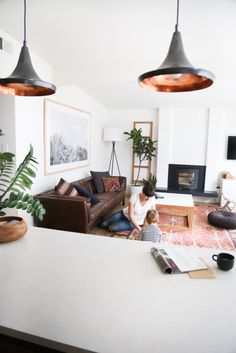 a woman sitting on the floor in front of a living room filled with furniture and potted plants