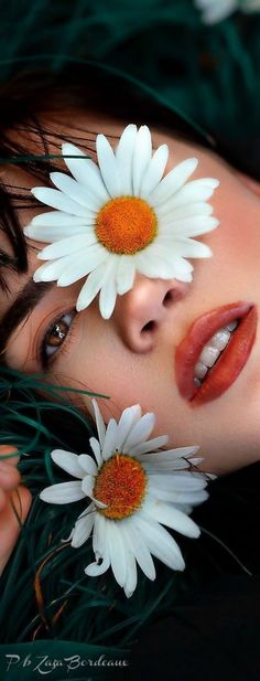 a woman with two daisies on her face and one flower in her hair is laying down