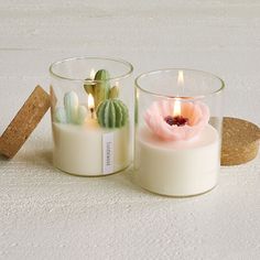 two candles are sitting next to each other on a white surface, one has a pink flower in it