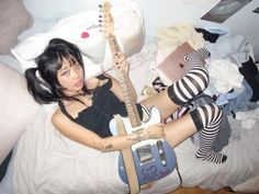 a woman laying on top of a bed with a guitar next to her legs and arm