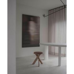 a white table and stool in front of a painting on the wall with curtains behind it