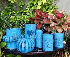 blue vases are lined up on a table in front of plants and potted plants