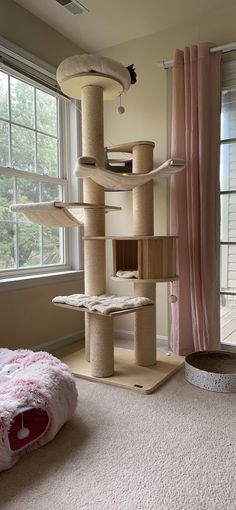 a cat tree in the corner of a room next to a window with pink curtains