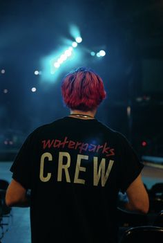 a man with red hair standing in front of a stage wearing a black crew t - shirt