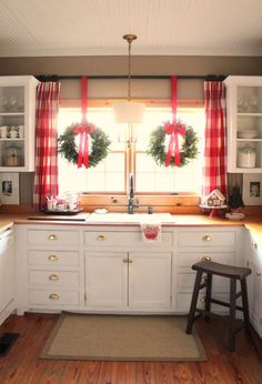 the kitchen is decorated for christmas with wreaths on the windowsill and red curtains