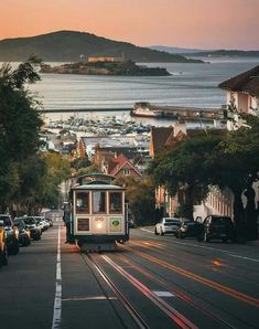 a trolley car traveling down the road next to some parked cars and buildings in front of an ocean