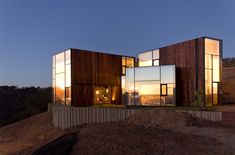 two modern houses sit on top of a hill at night with the sun setting in the background