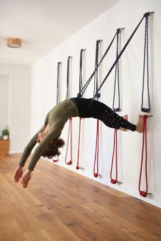 a woman hanging upside down on a rope in front of several ropes and poles, with her feet dangling off the wall