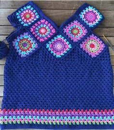 a blue crocheted top with flowers on the front and side, sitting on a wooden surface