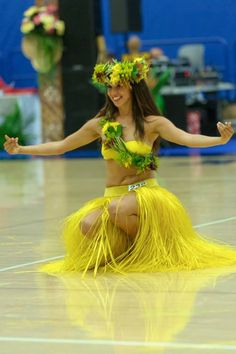 a woman in a yellow hula skirt dancing on a basketball court with her arms out