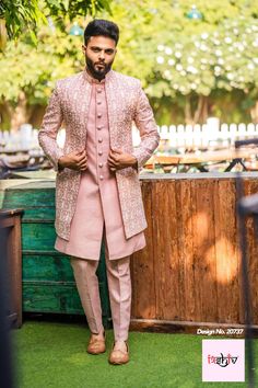 a man standing in front of a wooden fence wearing a pink suit and tan shoes