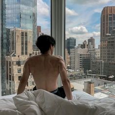 a shirtless man sitting on top of a bed in front of a large window