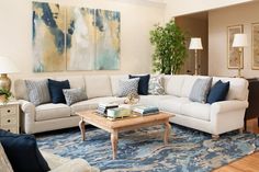 a living room with white couches and blue rugs in front of paintings on the wall