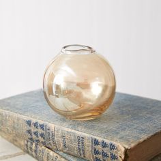 a clear glass vase sitting on top of two old book's cover books are stacked together