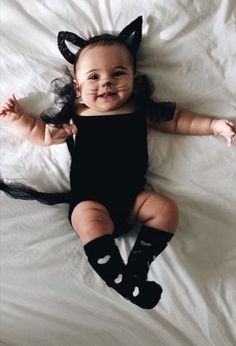 a baby dressed up as a cat laying on top of a white sheet covered bed