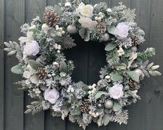 a wreath with white flowers and greenery hanging on a wooden wall next to a fence