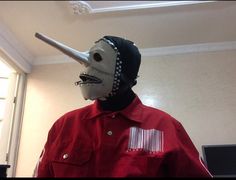 a man in a red shirt is wearing a mask and has his nose covered with metal spikes