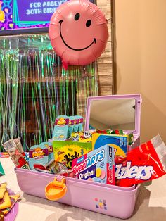 a pink suitcase filled with candy and other items sitting on a table next to a balloon