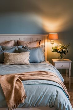 a bed with blue sheets and pillows in a bedroom next to a lamp on a table