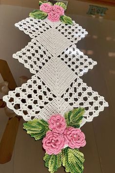 crocheted doily with pink flowers and green leaves on the edge, sitting on top of a table