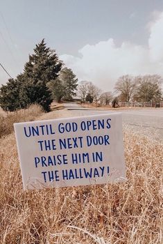 a sign that is in the middle of some dry grass near a road and trees