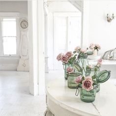 some pink flowers are sitting in mason jars on a white table with a mirror behind them