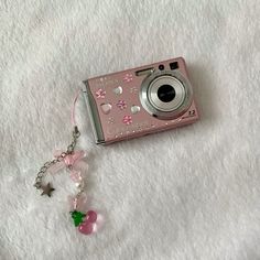 a pink camera sitting on top of a white blanket next to a keychain