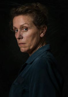 an older woman with blue eyes looking at the camera, against a black background and wearing a dark shirt