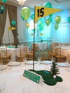 the table is set up for an event with balloons and decorations on it, including a golf green flag