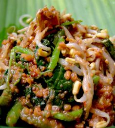 a green plate filled with noodles and vegetables on top of a leafy green surface