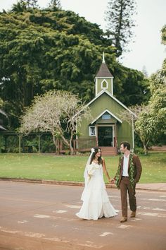 a bride and groom holding hands in front of a green building with a steeple