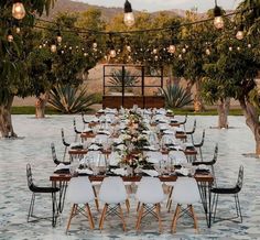 a long table is set up with white chairs and place settings for an outdoor dinner