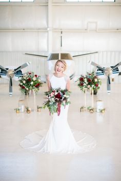 a woman in a white dress holding a bouquet and standing in front of an airplane