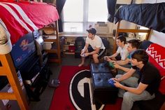 three young men sitting on top of bunk beds playing video games in a dorm room