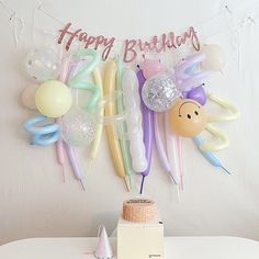 a birthday party with balloons, streamers and decorations on a white wall behind a cake